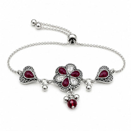 An antique silver adjustable slider bracelet with a central flower, two hearts, ruby-red pear stones, and dangling beads on