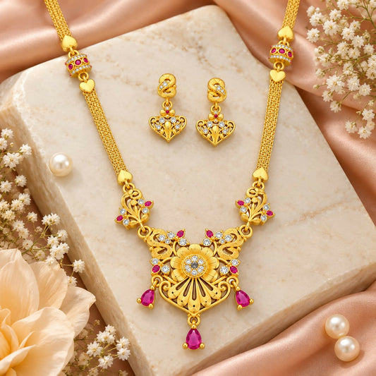 Golden necklace and matching earrings with ruby and white stones displayed on a marble slab.
