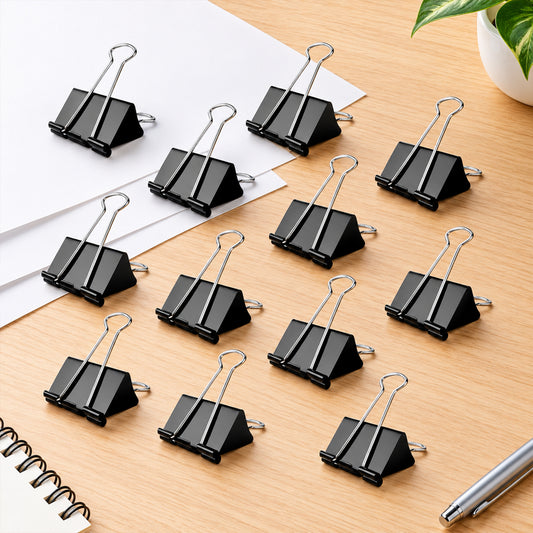 Twelve black binder clips with silver handles are arranged on white paper on a wooden surface.