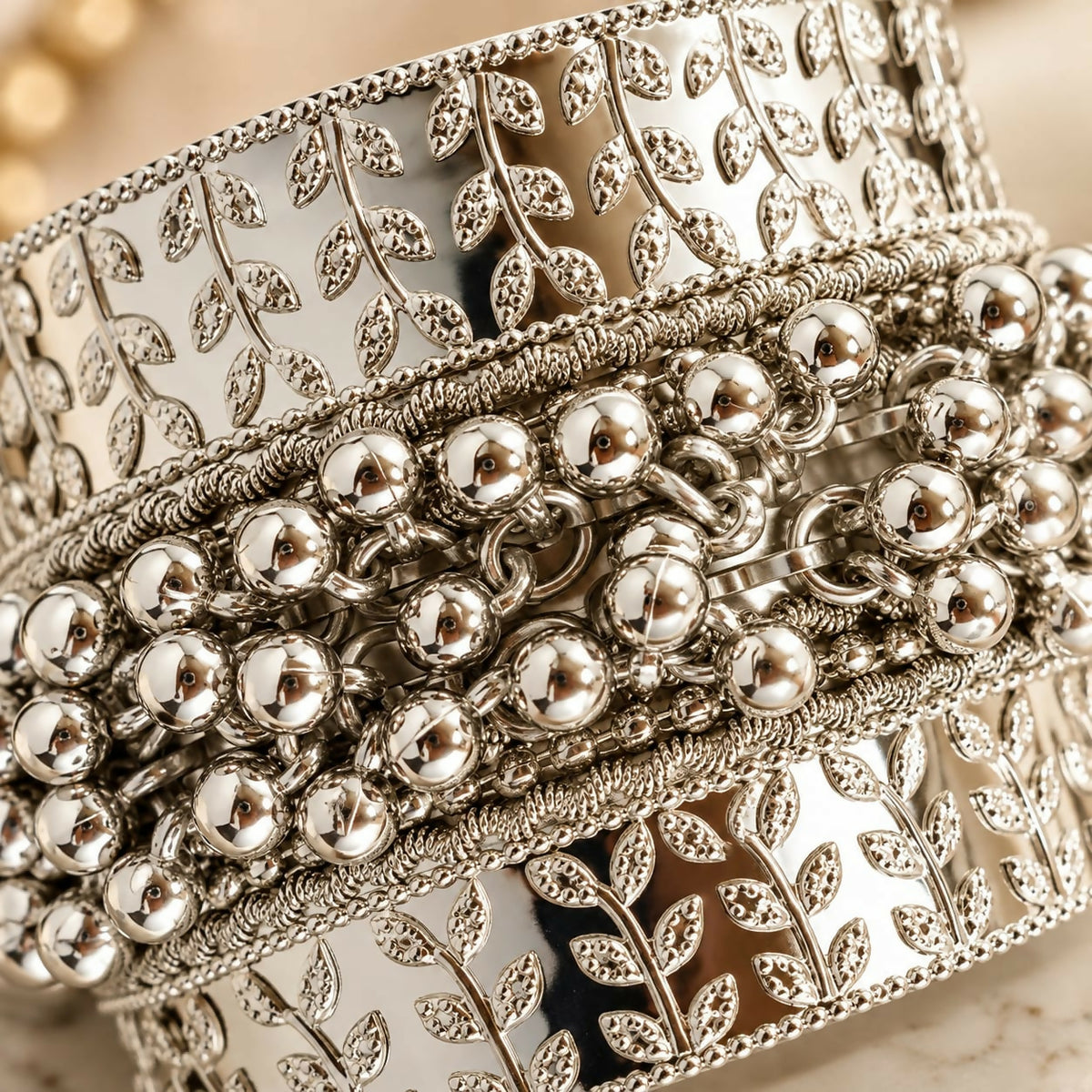 Close-up view of a silver-tone kada bangle showing intricate leaf patterns and a central design of multiple ghungroo beads.