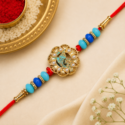 A gold Ganesha charm with blue enamel and pearl accents is centered on a red thread with blue and turquoise beads.