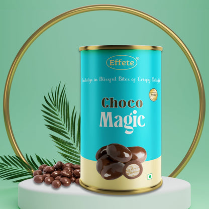 A blue and gold cylindrical container of chocolate balls on a white pedestal, with a gold ring and palm leaf.