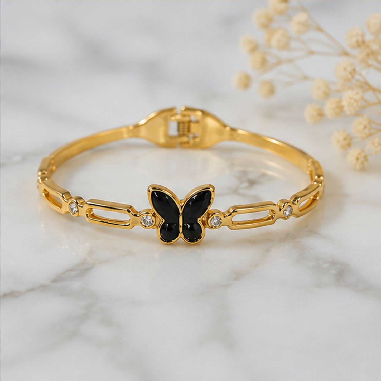 A gold-tone bracelet with a black butterfly charm and crystal accents rests on a white marble surface.