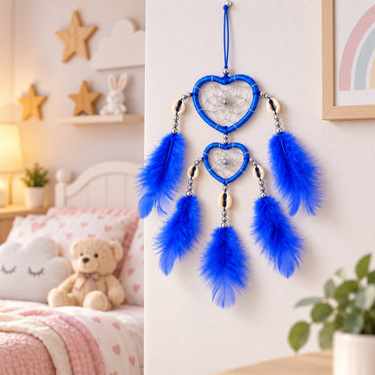 A blue heart-shaped dream catcher with feathers hangs on a white wall in a child's bedroom with a teddy bear and bed visible.
