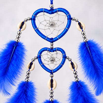 Close-up of the blue heart-shaped dream catcher, showing intricate web patterns, silver beads, and cowrie shells.