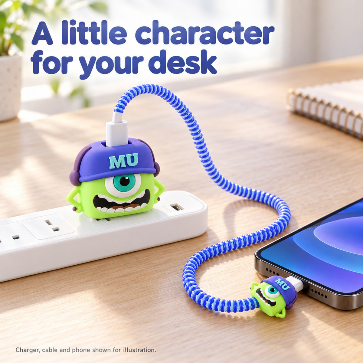 A green Mike Wazowski silicone charger cover and cable protector set charging a phone on a wooden desk.