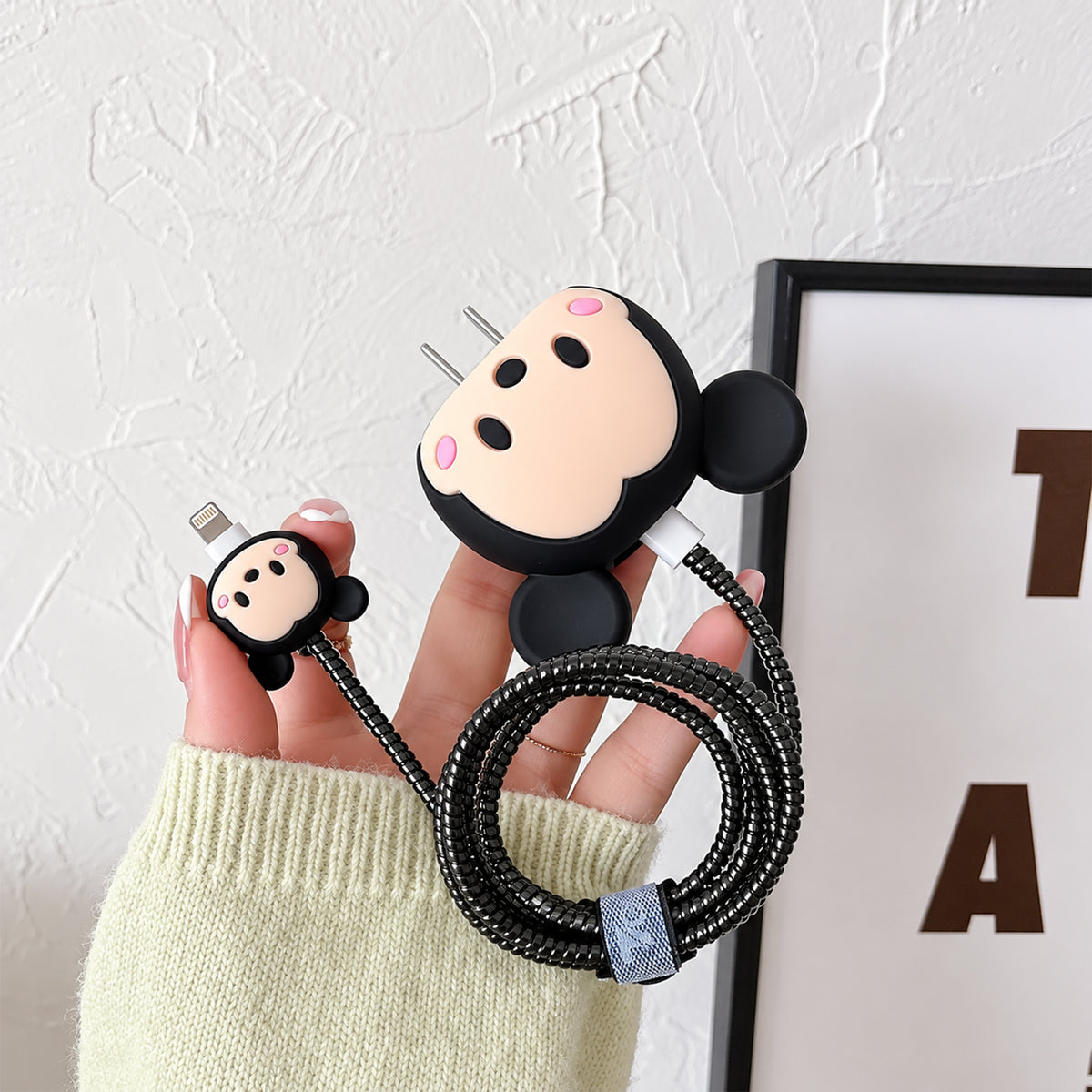 A hand holds a black Mickey Mouse silicone charger cover with a matching cable protector and coiled cable.