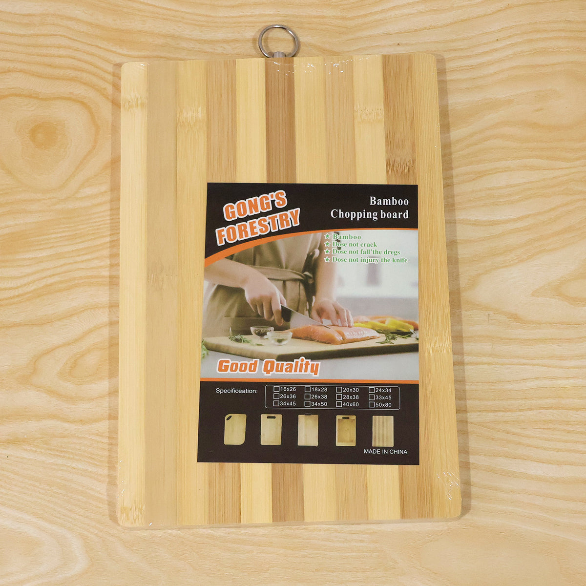 A bamboo chopping board with a product label featuring a person cutting food and various size options.