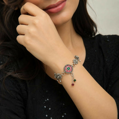 A woman wears the oxidized silver bracelet, featuring a red and green enamel mandala and floral links, on her wrist.
