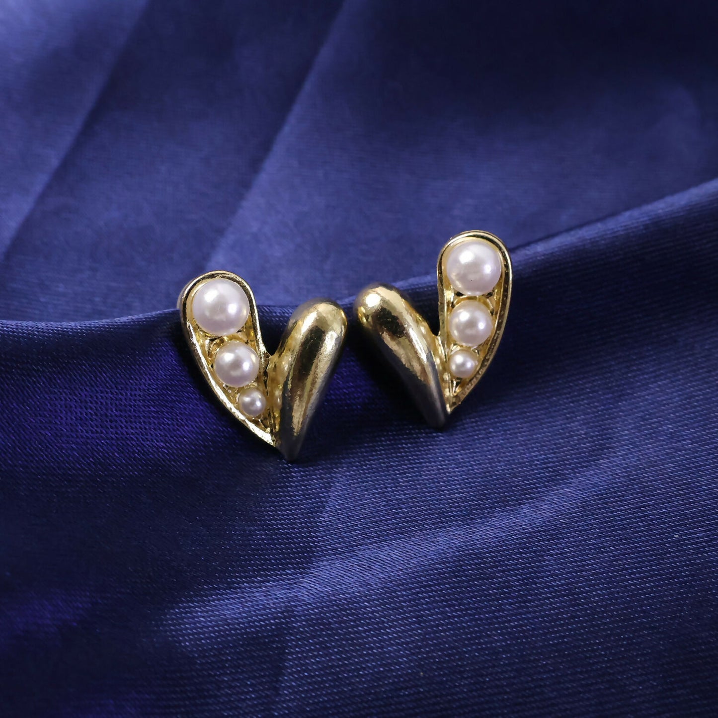 Pair of gold pearl heart stud earrings displayed on dark surface