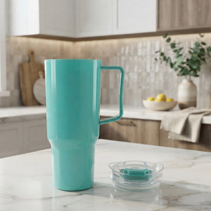An aqua blue tumbler with a handle stands next to its clear lid on a marble kitchen counter with blurred cabinets in the