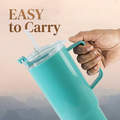 A hand holds the handle of an aqua blue tumbler with a clear lid and straw against a blurred, warm-toned background with the