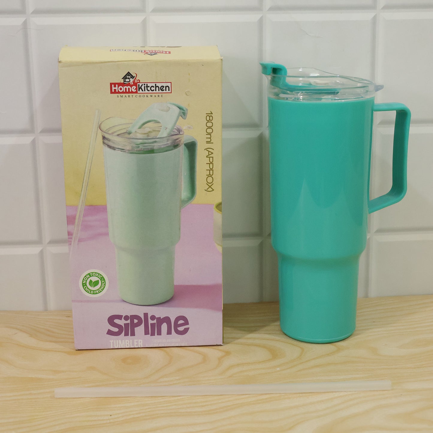 An aqua blue tumbler with a handle, clear lid, and straw stands next to its product box and a loose straw on a wooden