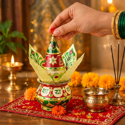 A hand places a red tassel on a colorful kalash with golden leaves, surrounded by lit lamps and incense.