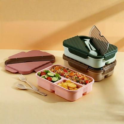 A pink bento lunch box with three compartments filled with rice, salad, and chips, next to a fork and spoon.