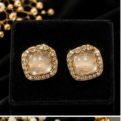 Two identical square stud earrings, featuring clear stones and brilliant gem edges, are displayed on a black velvet stand.