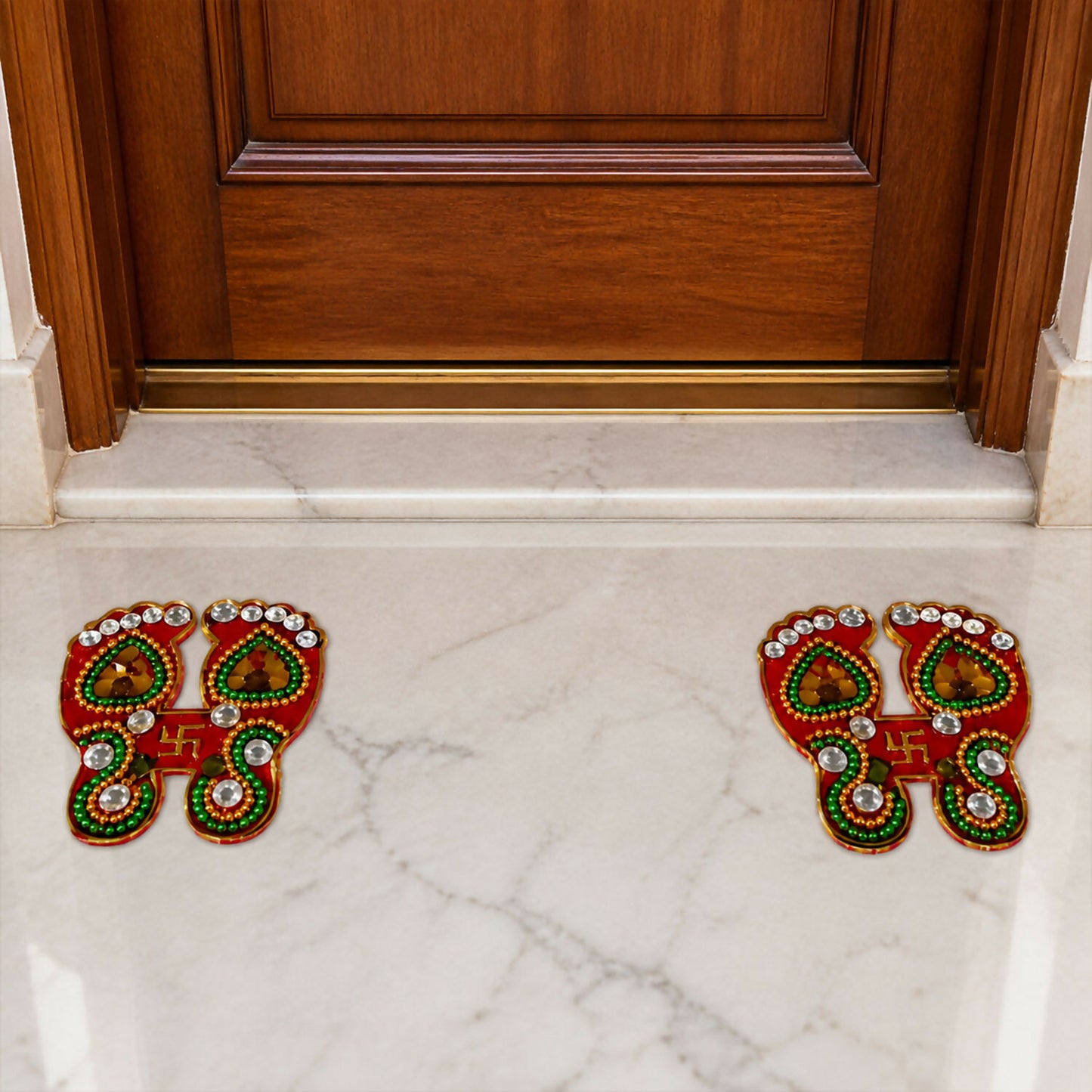 Two pairs of red and gold Laxmi Charan Paduka stickers with green and white embellishments on a white marble floor.