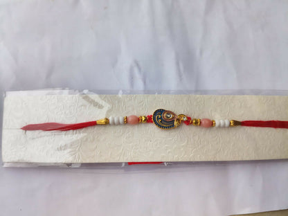 A red, blue, and gold peacock charm bracelet is packaged in clear plastic on a white textured card, against a white