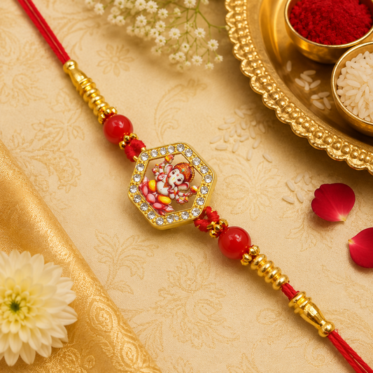 A red thread bracelet with a gold-framed Ganesha figure charm and red beads is displayed on a gold patterned fabric.