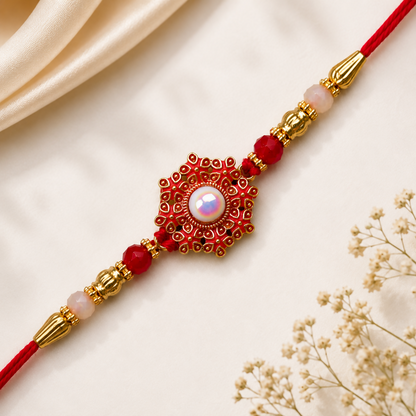 A red and gold beaded bracelet with a central red floral medallion and white pearl, on a white background with draped fabric.