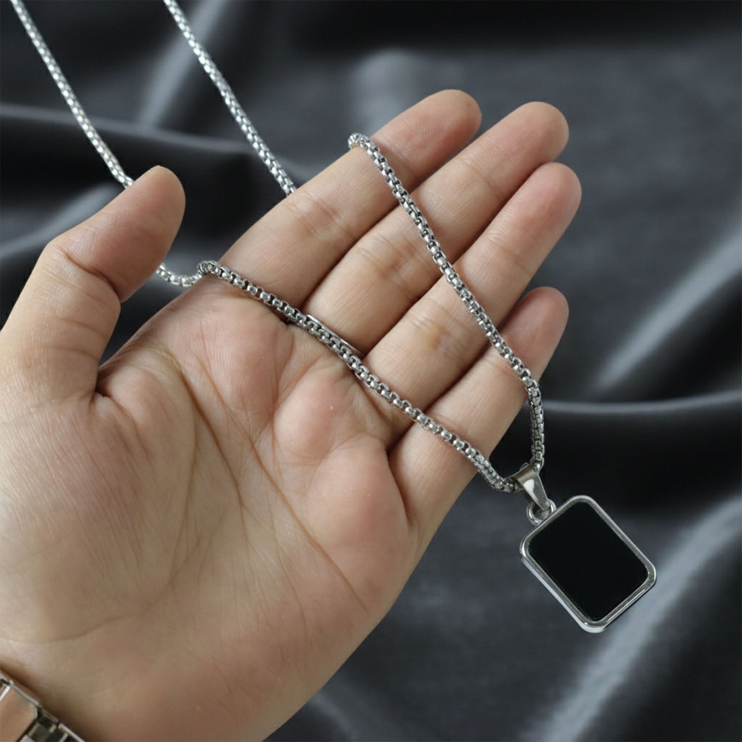 Black rectangle pendant with polished metal frame on stainless-steel chain