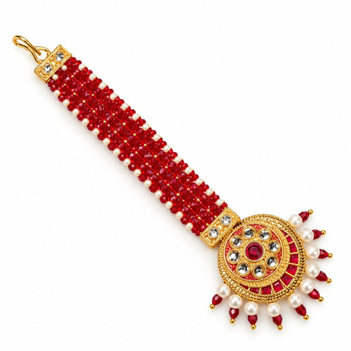 A gold-plated maang tikka with red and white beads, featuring a circular pendant with a central red gem, is displayed on a