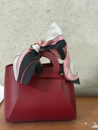 Stylish maroon mini handbag with ribbon bow on a table