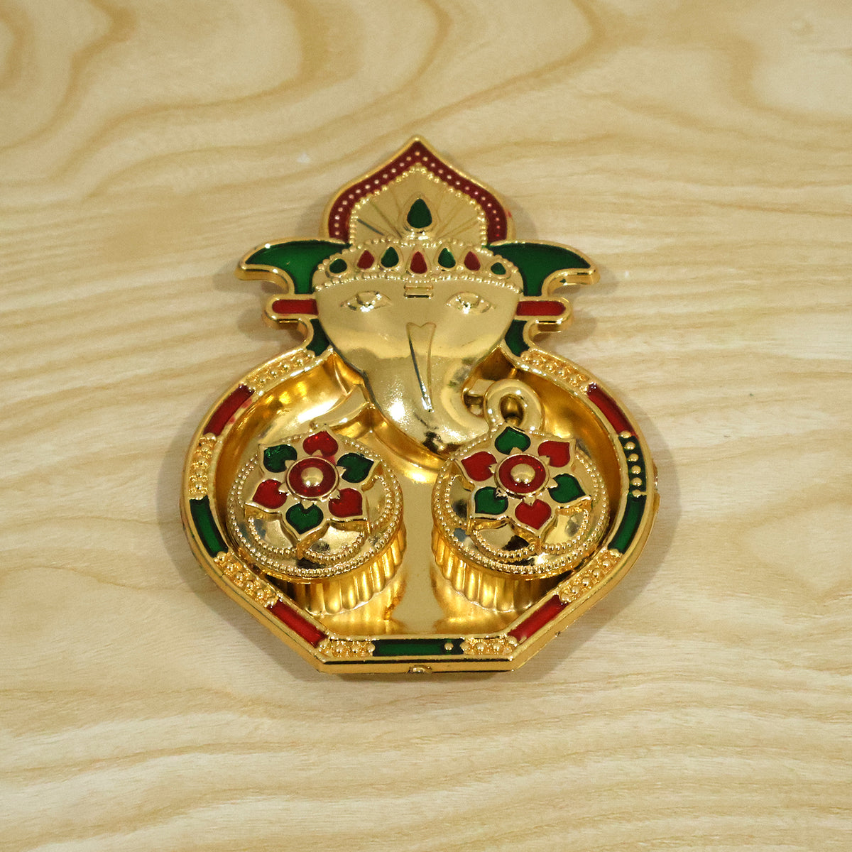 A golden Ganesha-shaped kumkum holder with red and green enamel details on a light wooden surface.