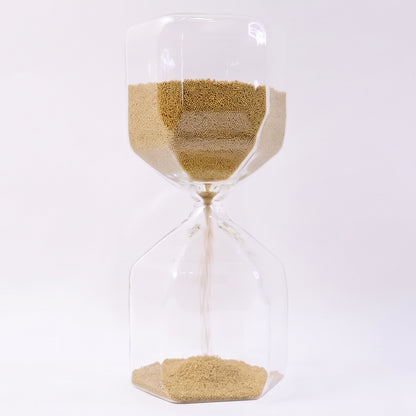 Close-up of fine yellow sand flowing in glass hourglass timer
