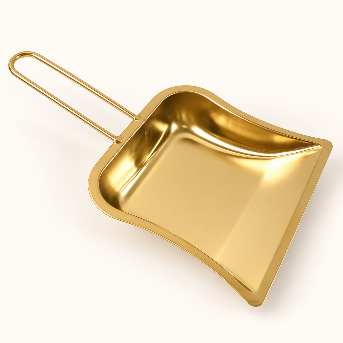 A gleaming gold-tone metal dustpan with a simple loop handle is angled on a plain white surface.
