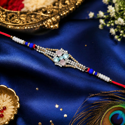 A red thread bracelet with a central diamond-studded floral design featuring pink and blue-green crystals, on a blue silk
