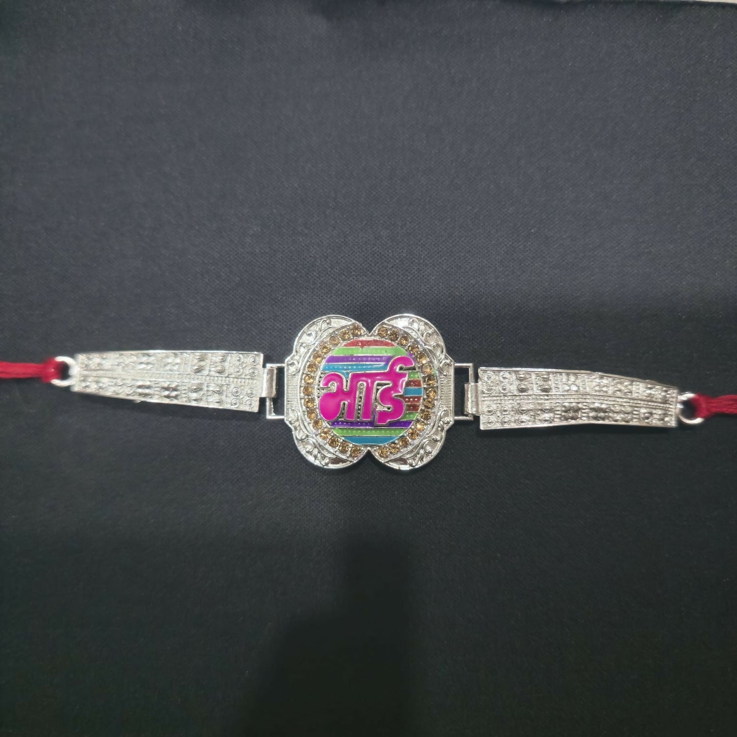 The silver-finished Bhai bracelet with a colorful striped centerpiece and textured bands is presented on a plain black