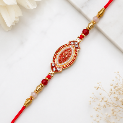 A red and gold bracelet with an oval centerpiece, adorned with white beads and red stones, lies on a white marble surface
