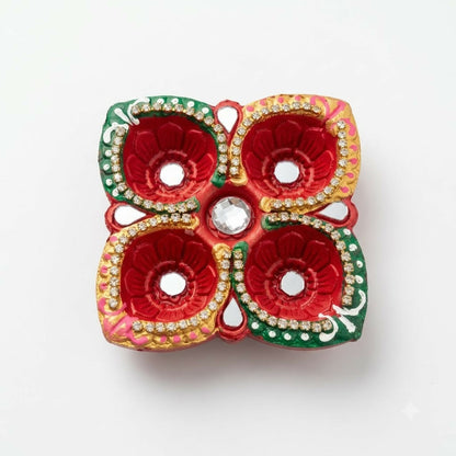 A top-down view of a red, green, and gold four-cup diya with mirror details and a central clear gem on a white background.