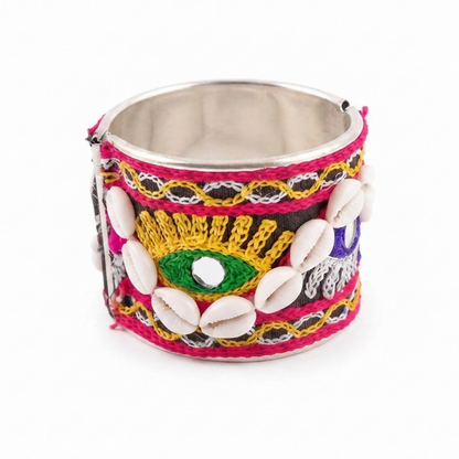 A wide silver cuff bangle with black fabric, vibrant embroidery, and cowrie shells on a white background.