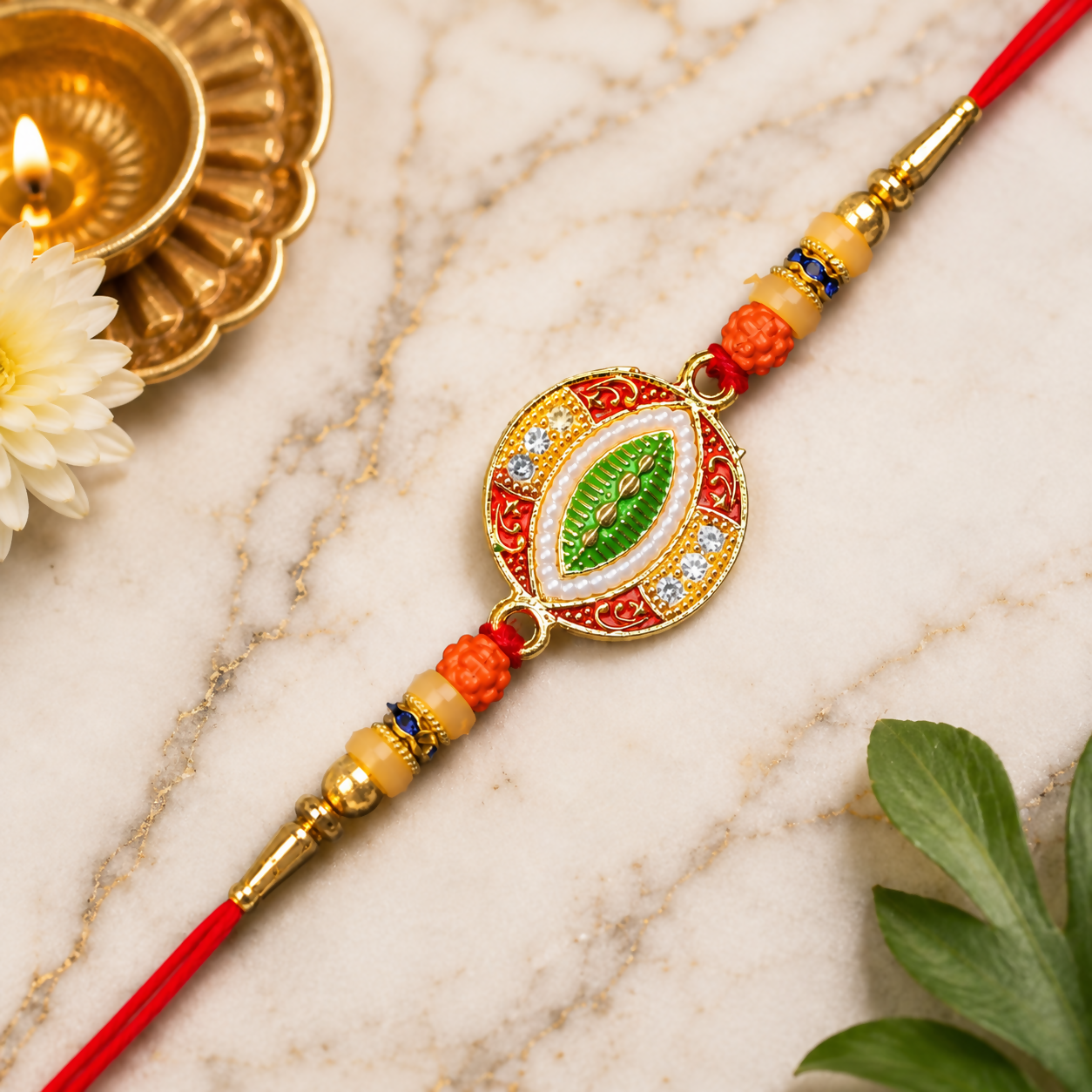 A red and gold bracelet with orange beads, a central green leaf design, and white stones on a white marble surface with a