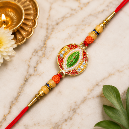 A red and gold bracelet with orange beads, a central green leaf design, and white stones on a white marble surface with a