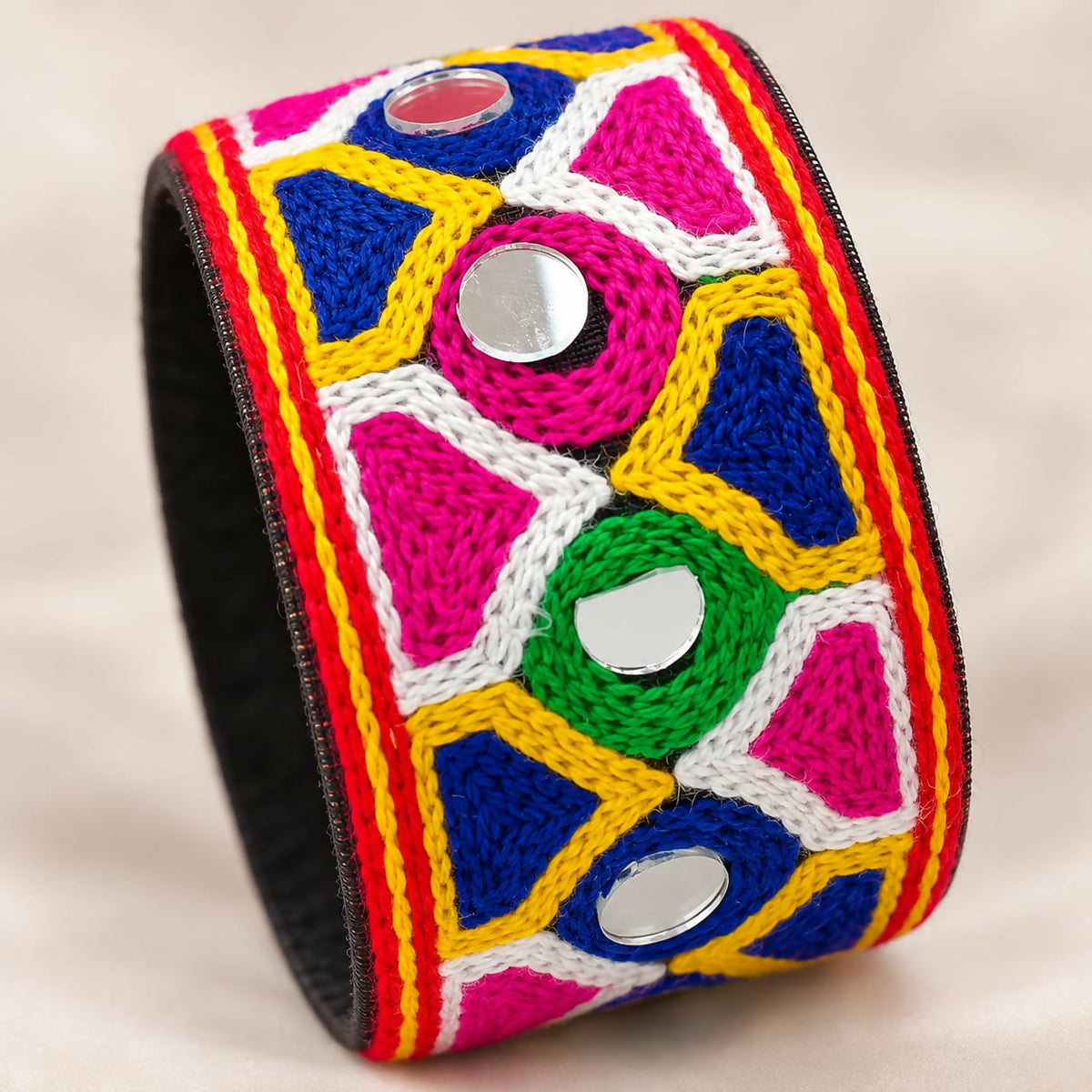 A bright, intricately embroidered cuff bracelet with mirror details rests on a soft, light-colored fabric.