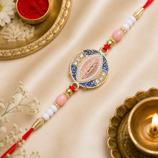A blue, pink, and gold Rakhi with a central oval design, surrounded by small white stones and pearls, rests on a gold satin