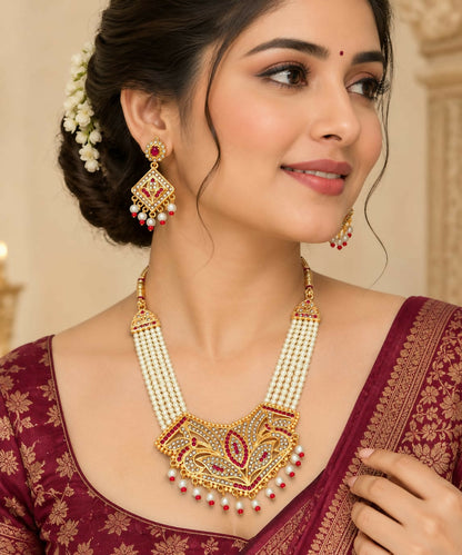 A woman models a pearl necklace with a detailed ruby-studded pendant and matching dangling earrings, wearing a maroon