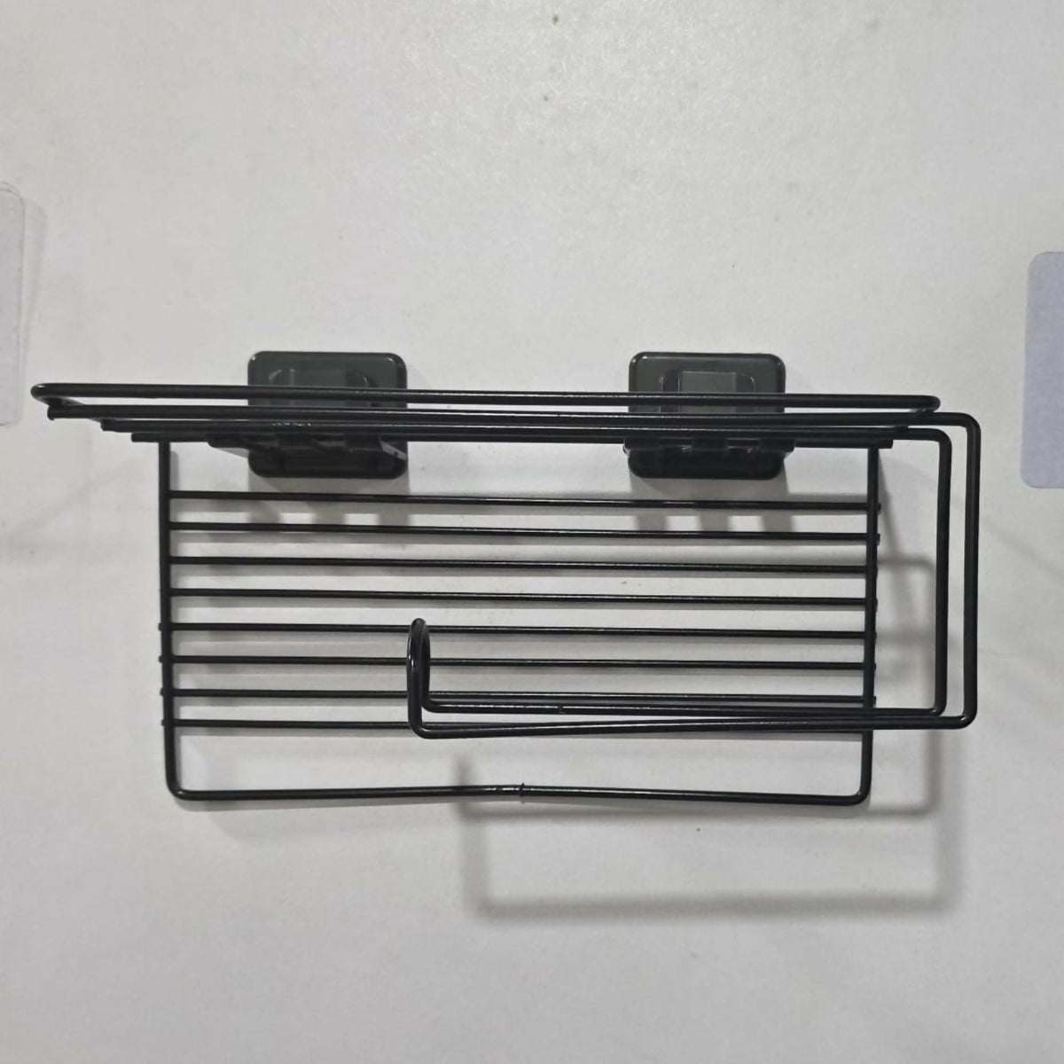 The empty black metal toilet paper holder, showing its wire design and two clear adhesive mounting pads.