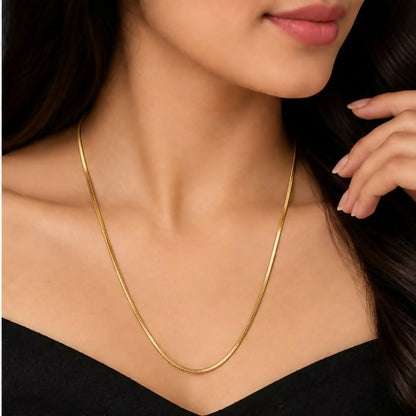 A person with long dark hair wears a shiny gold-tone snake chain necklace against a black top.