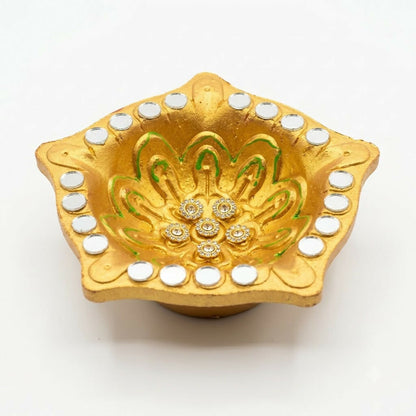 A close-up of a gold star-shaped diya with green painted details, small mirrors, and rhinestone flowers.