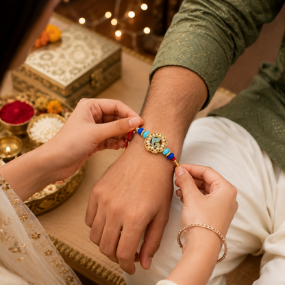 A person's hands tie the Ganesha charm bracelet onto another person's wrist, with festive items in the background.