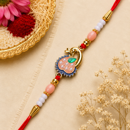 A red thread with a gold peacock charm, pink and white beads, and gold accents, next to a gold plate with flowers.