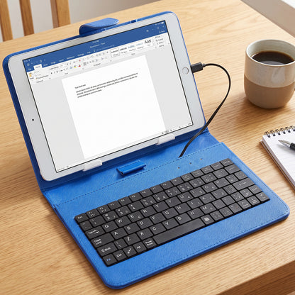 A blue PU leather case with a tablet and wired keyboard sits on a wooden table next to a coffee mug.