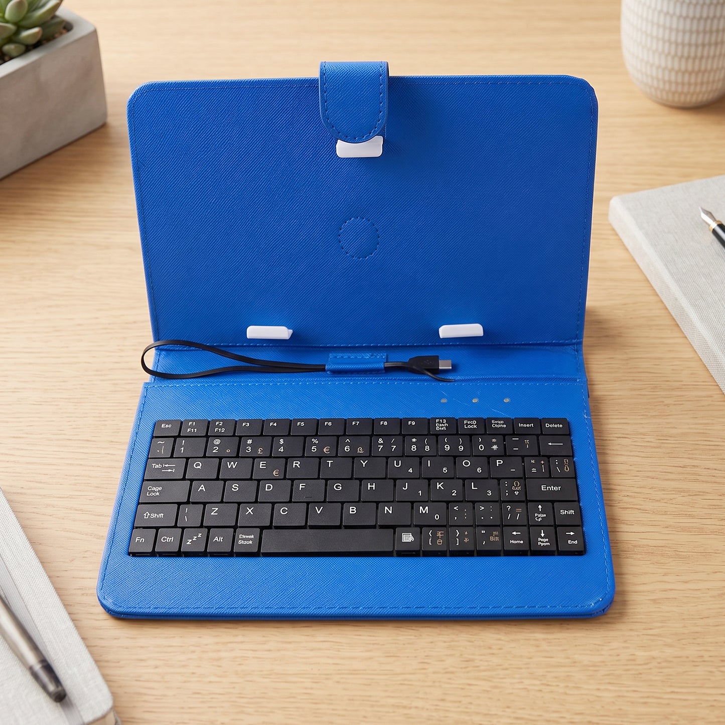 An open blue PU leather case reveals a black wired keyboard and tablet stand on a wooden surface.