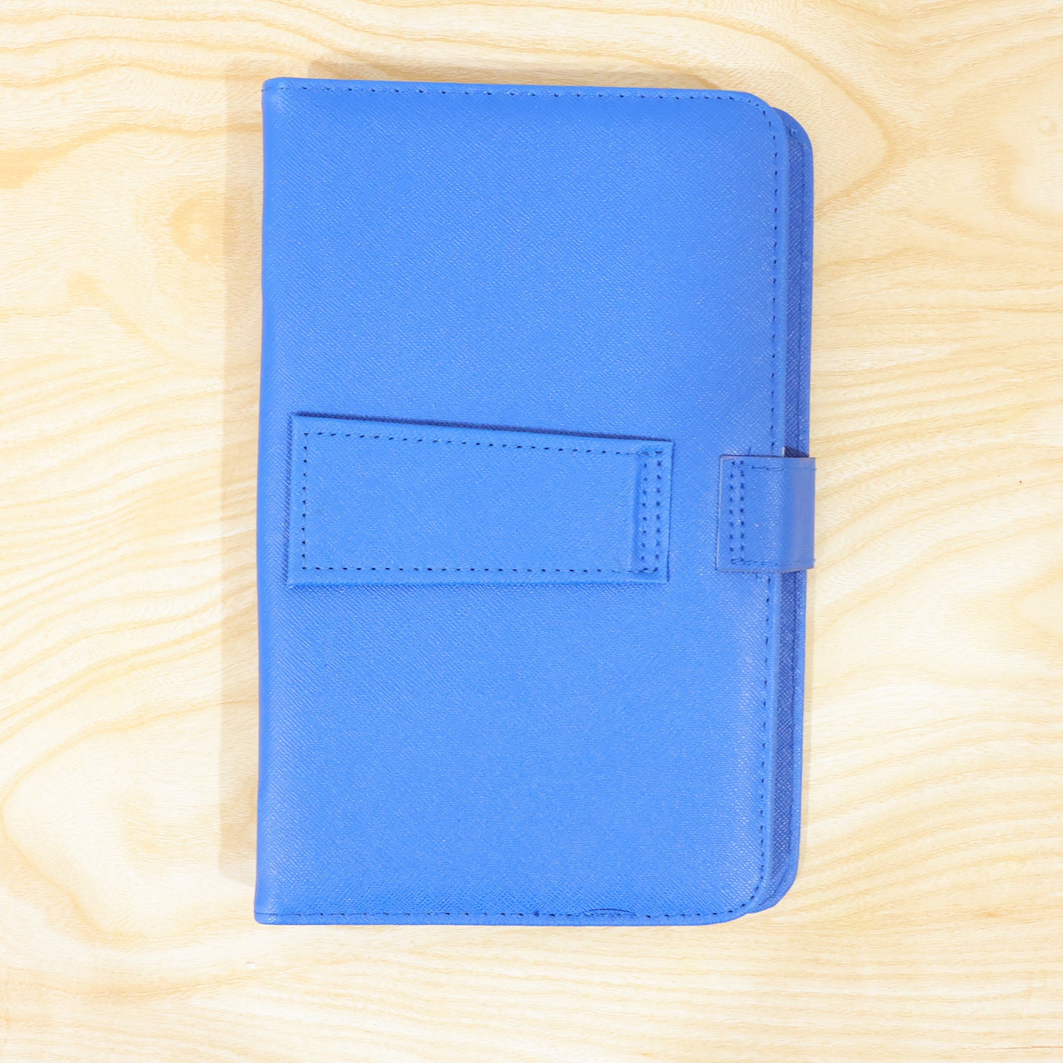 A closed blue PU leather tablet case with a flap closure is centered on a light wooden background.