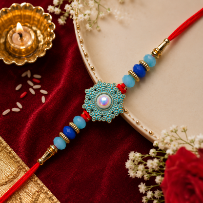A red thread with a teal and gold medallion, featuring a central pearl, is on a red velvet cloth with a lit candle.