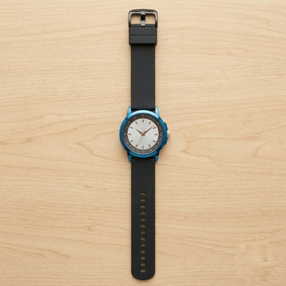 A blue watch with a white face, gold hands, and a black strap is viewed from above on a light wood surface.